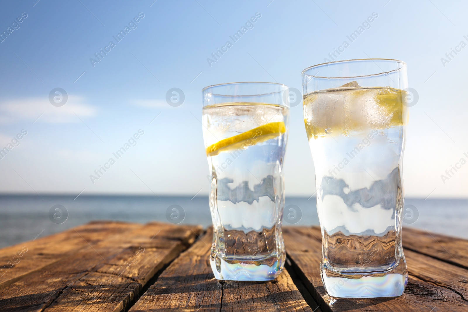 Photo of Wooden table with glasses of refreshing lemon drink on hot summer day outdoors, space for text