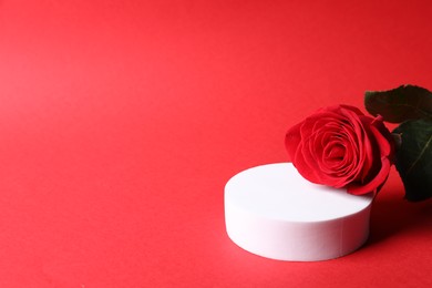 Photo of Stylish presentation for product. Round podium and beautiful rose on red background, space for text