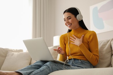 Woman with laptop and headphones sitting on sofa at home