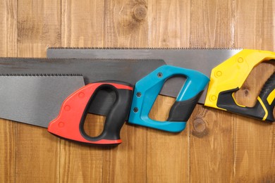 Photo of Saws with colorful handles on wooden background, flat lay