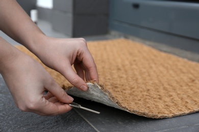 Photo of Woman hiding key under door mat, closeup. Space for text