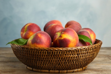 Photo of Wicker bowl with tasty peaches on wooden table against blue background