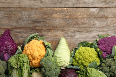 Photo of Different cabbages on wooden table, top view. Healthy food