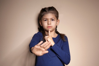 Photo of Little girl showing HUSH gesture in sign language on color background