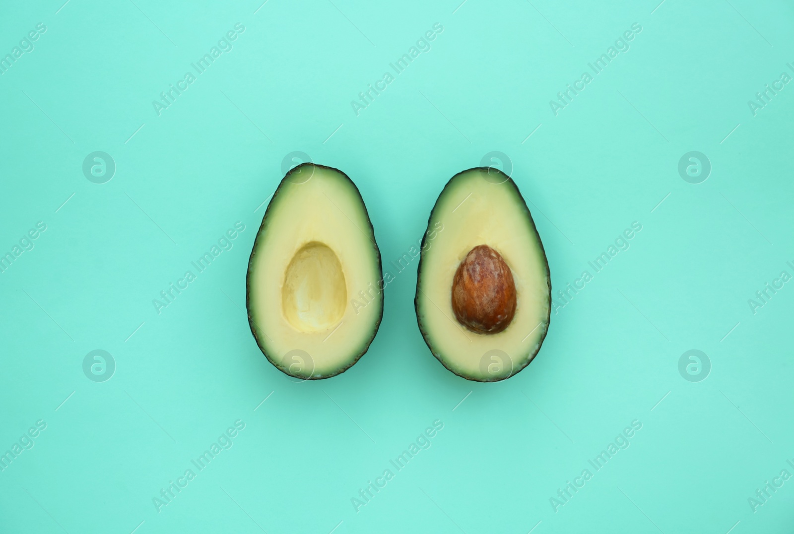 Photo of Halves of tasty fresh avocados on turquoise background, flat lay