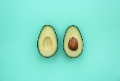 Halves of tasty fresh avocados on turquoise background, flat lay