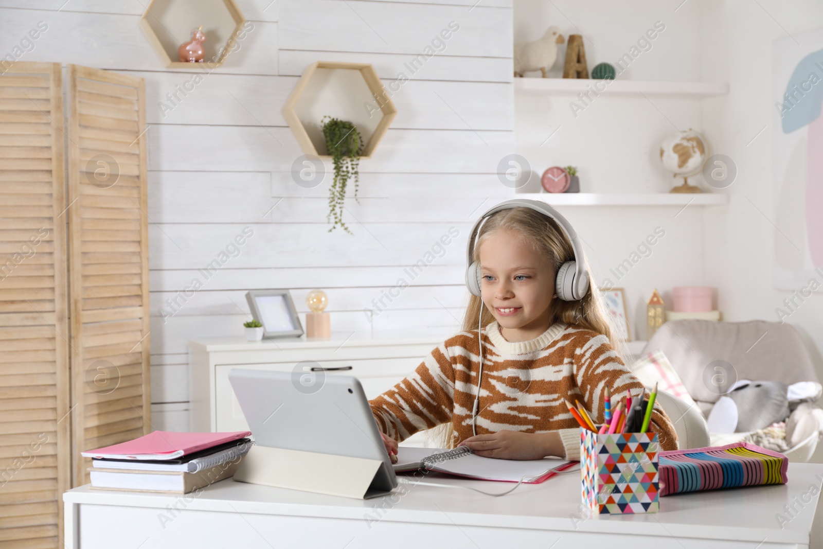 Photo of Cute little girl with modern tablet studying online at home, space for text. E-learning