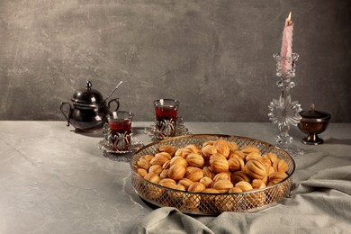 Photo of Delicious walnut shaped cookies, burning candle and cups of tea on grey table, space for text. Tasty pastry carrying nostalgic home atmosphere