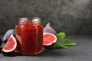 Photo of Glass jar with tasty sweet jam, green leaf and fresh figs on grey table. Space for text