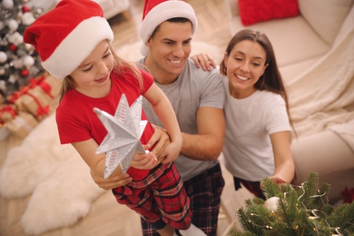 Family decorating Christmas tree with star topper in room, above view