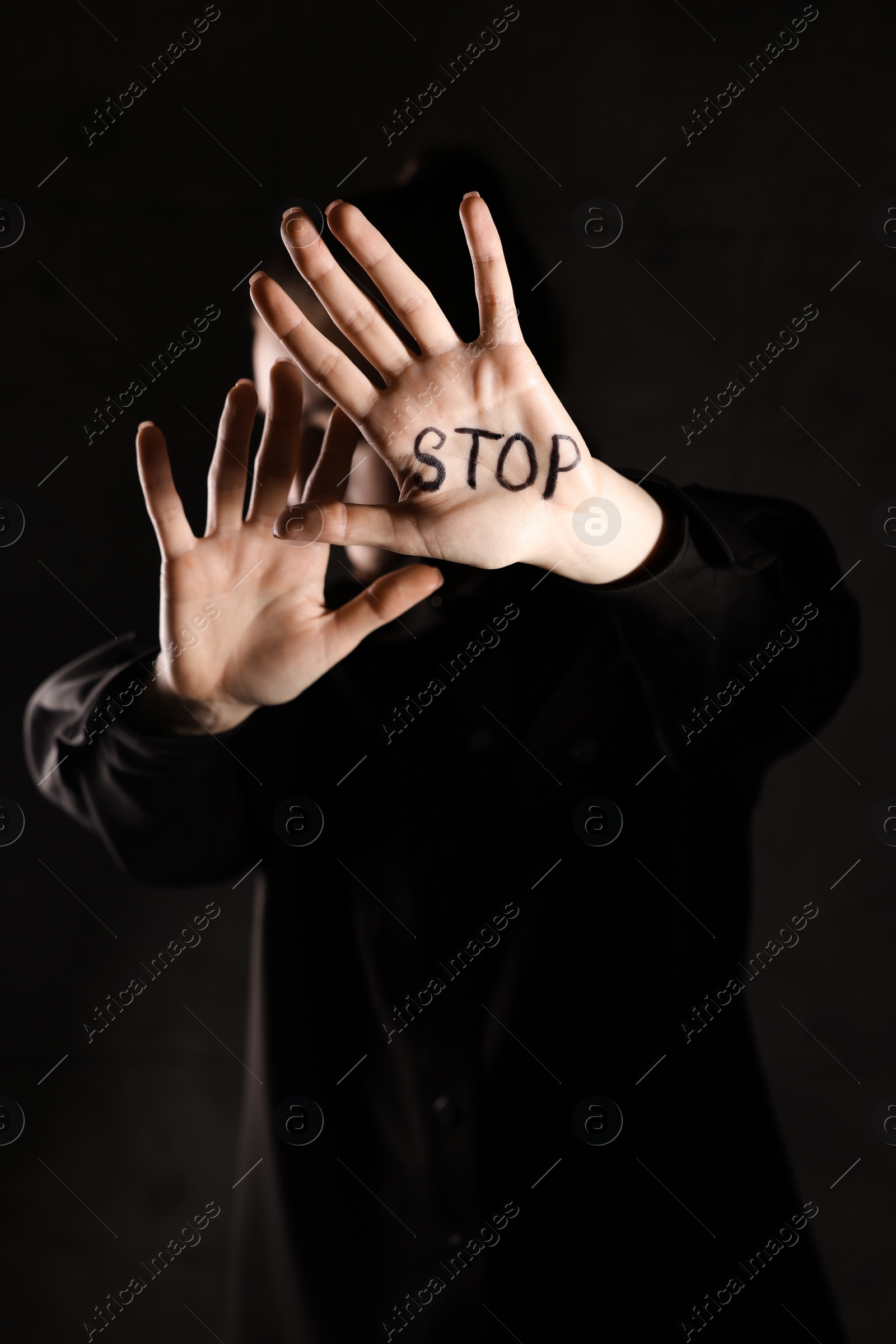 Photo of Woman with word Stop written on hand against dark background, closeup. Domestic violence concept