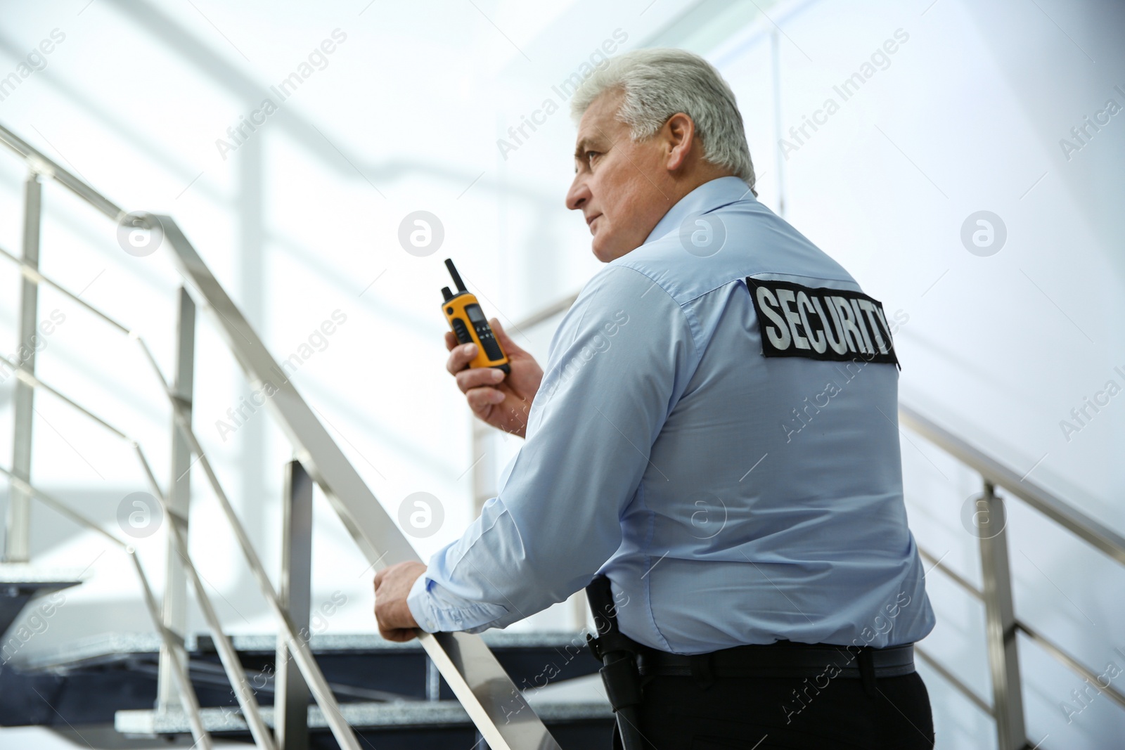 Photo of Professional security guard with portable radio set on stairs indoors