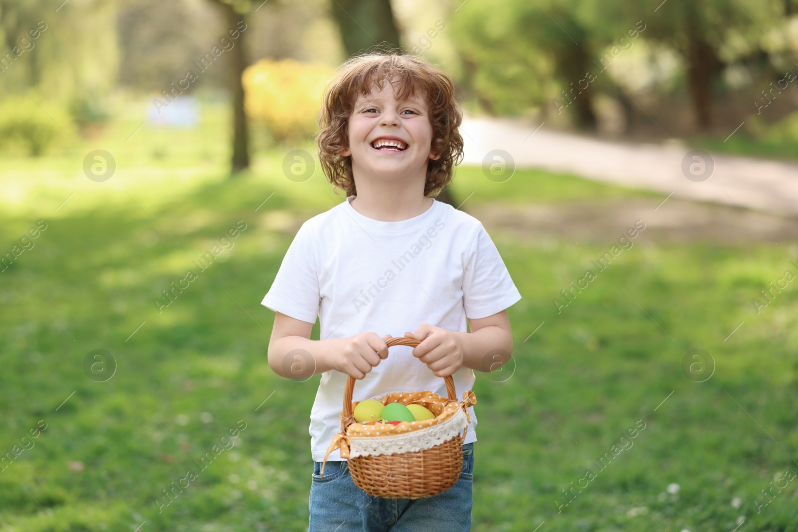 Photo of Easter celebration. Cute little boy holding wicker basket with painted eggs outdoors