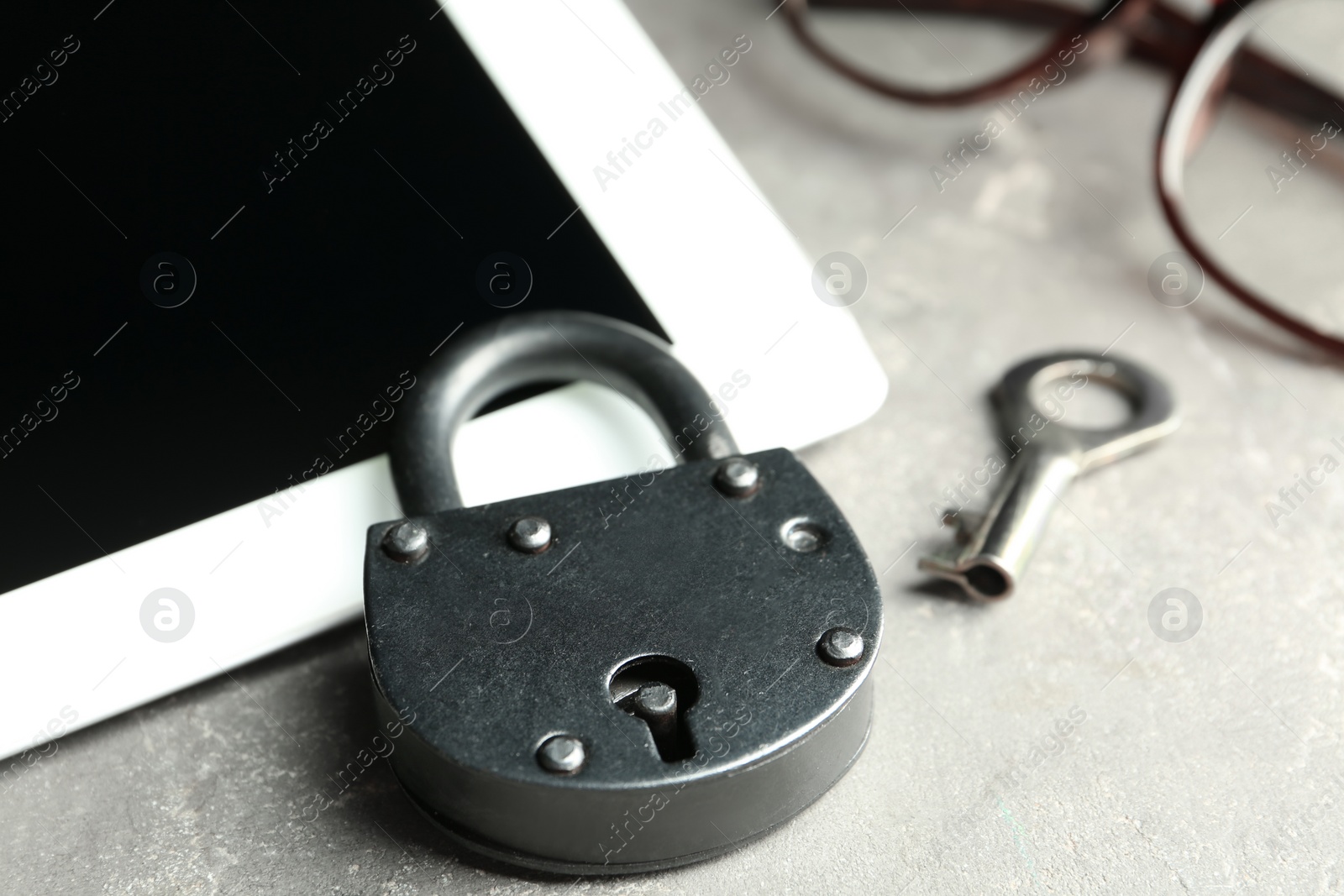 Photo of Vintage metal lock with key and tablet on grey table, closeup. Protection from cyber attack