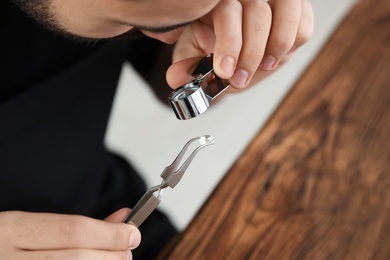 Male jeweler evaluating precious gemstone at table in workshop, closeup