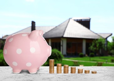 Image of Piggy bank and stacked coins on stone surface and blurred view of beautiful house. Mortgage concept