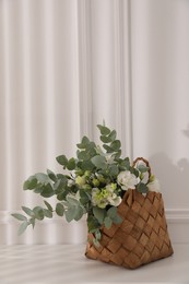 Stylish wicker basket with bouquet on white table indoors, space for text