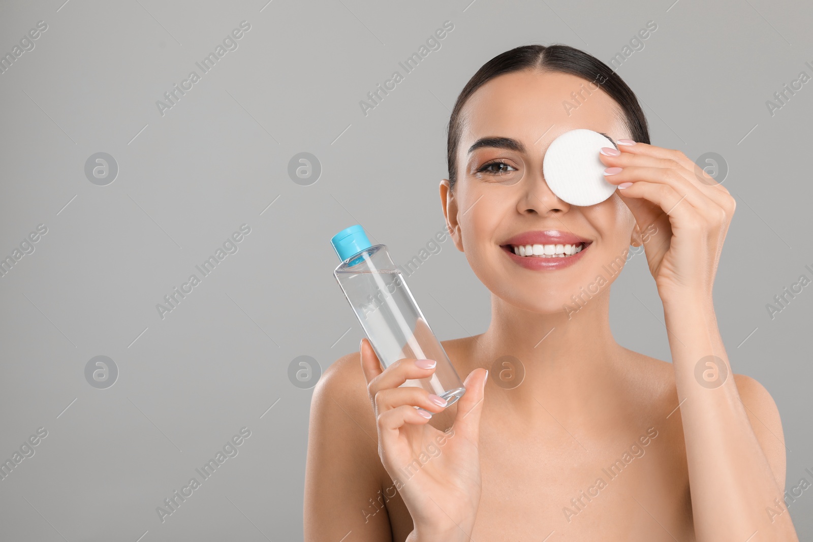 Photo of Beautiful woman removing makeup with cotton pad on light grey background, space for text
