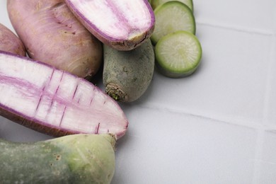 Purple and green daikon radishes on white tiled table, closeup. Space for text