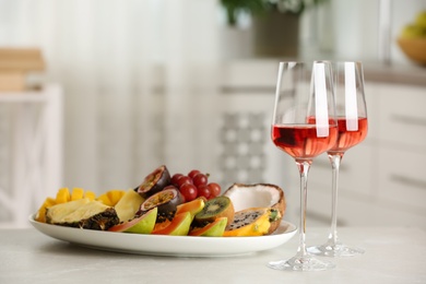 Delicious exotic fruits and glasses of wine on white table indoors