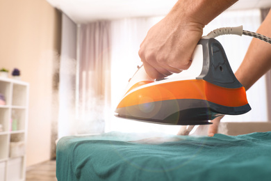 Man ironing clothes on board at home, closeup