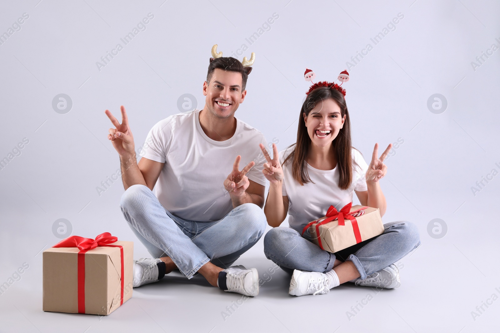 Photo of Beautiful happy couple in Christmas headbands with gifts having fun on light background