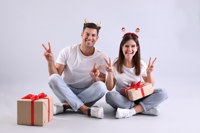Photo of Beautiful happy couple in Christmas headbands with gifts having fun on light background