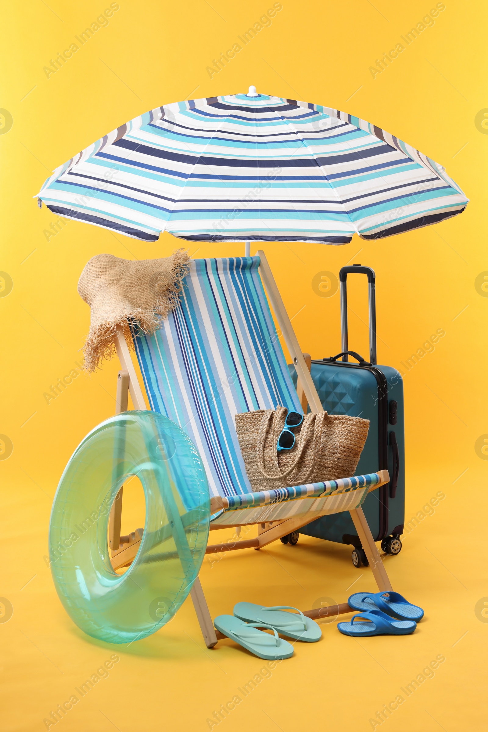 Deck chair, umbrella, suitcase and beach accessories on yellow background. Summer vacation Photo of Deck chair, umbrella, suitcase and beach accessories on yellow background. Summer vacation