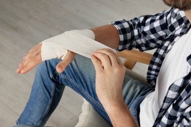 Man applying medical bandage onto hand indoors, closeup