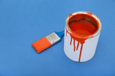 Photo of Can of orange paint and brush on blue background. Space for text
