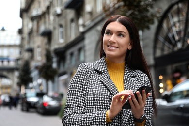 Photo of Beautiful woman in stylish suit using smartphone on city street