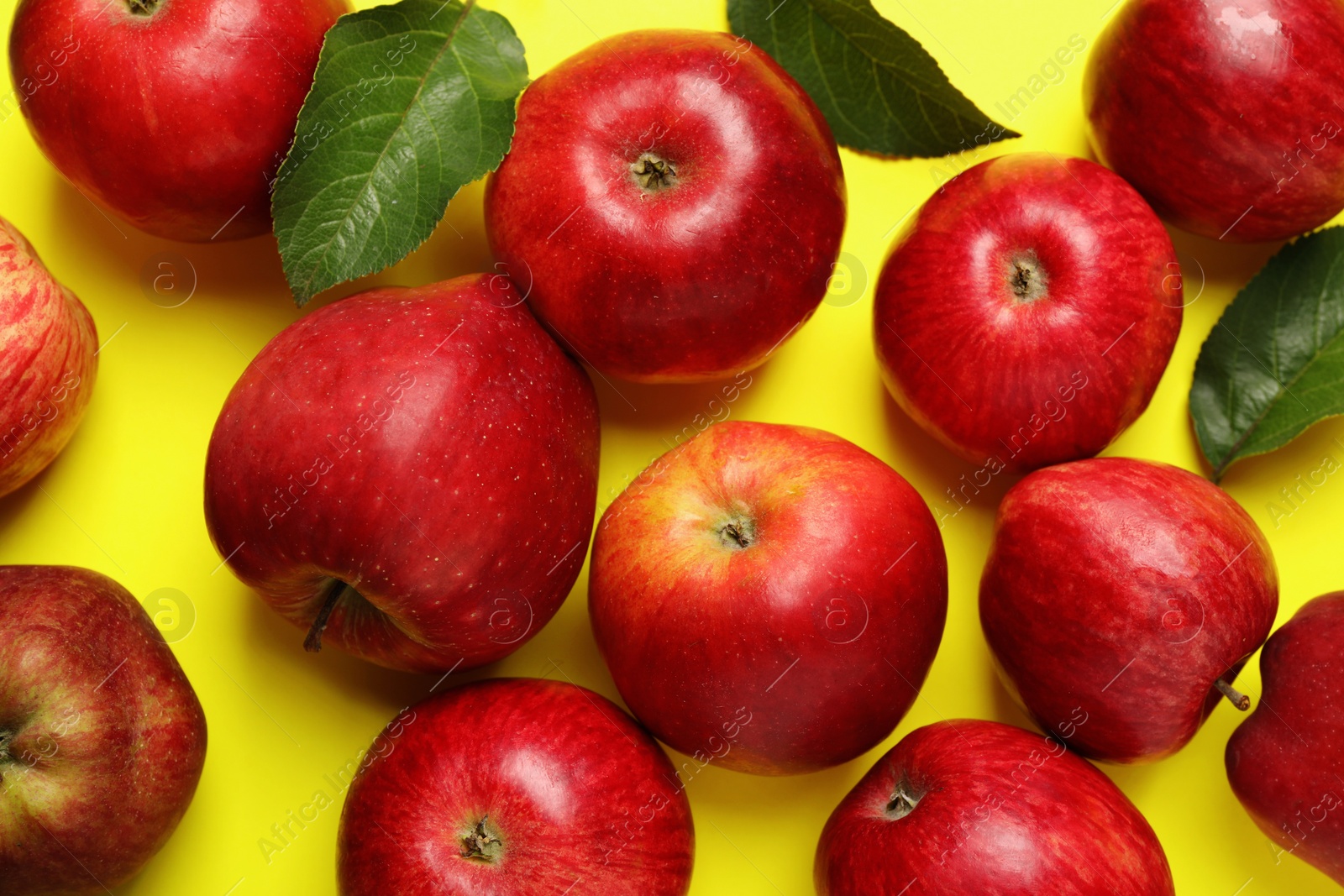 Photo of Ripe red apples and green leaves on yellow background, flat lay