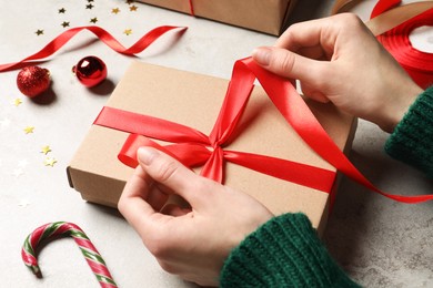 Photo of Woman decorating gift box at light grey table, closeup. Christmas present