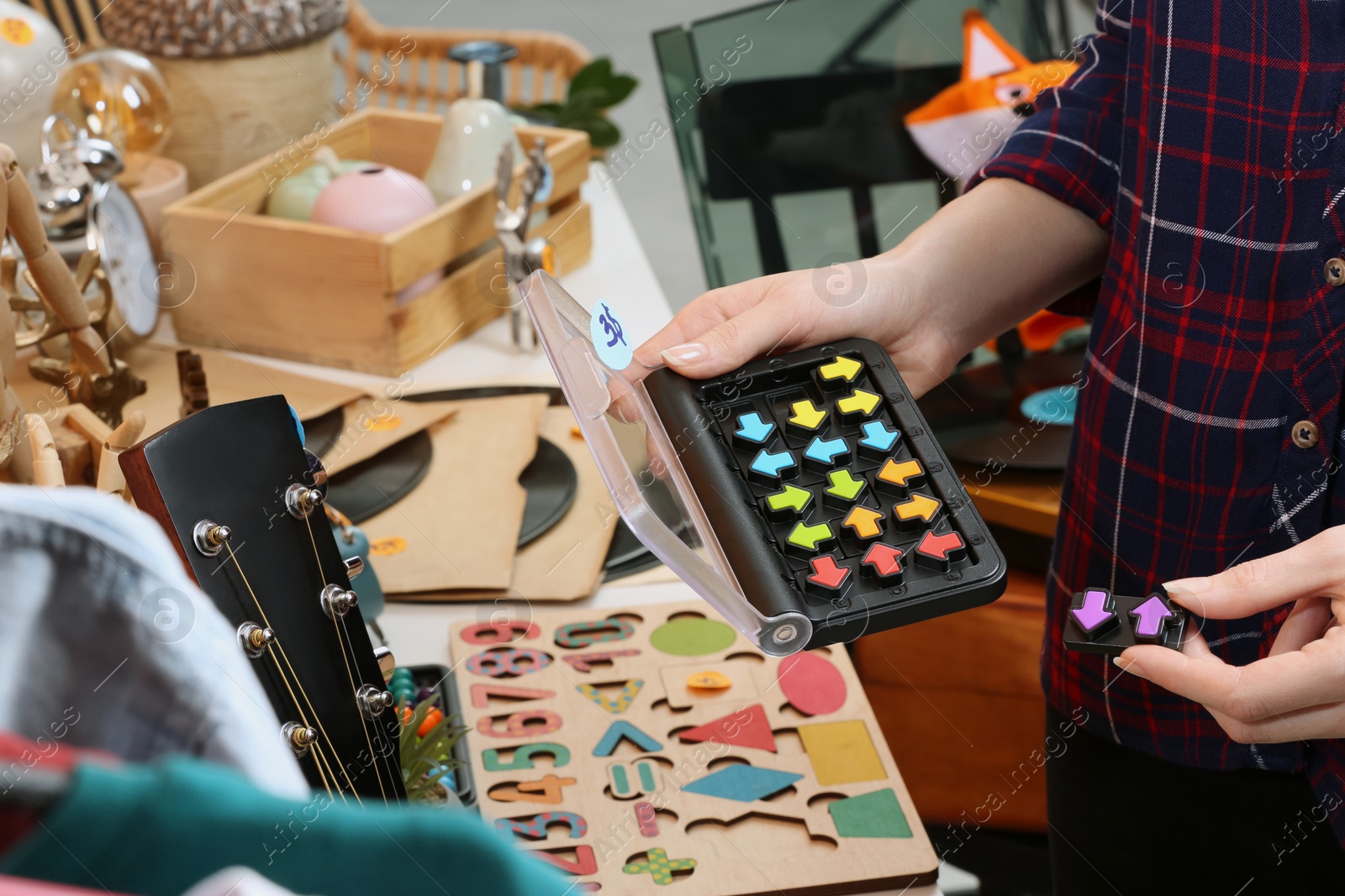 Photo of Woman holding smart game IQ near table with different stuff indoors, closeup. Garage sale