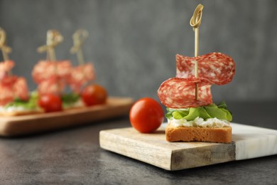 Photo of Tasty canapes with salami, greens, cream cheese and tomatoes on grey table, closeup. Space for text