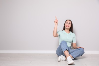 Photo of Young woman sitting on floor near light grey wall indoors. Space for text