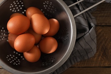 Photo of Chicken eggs in colander and napkin on wooden table, top view