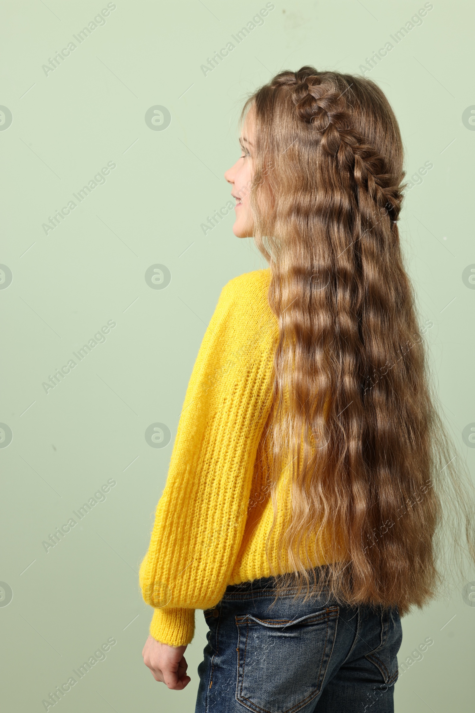Photo of Cute little girl with braided hair on light green background