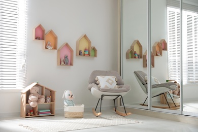 Photo of Cute children's room with house shaped shelves and rocking chair. Interior design