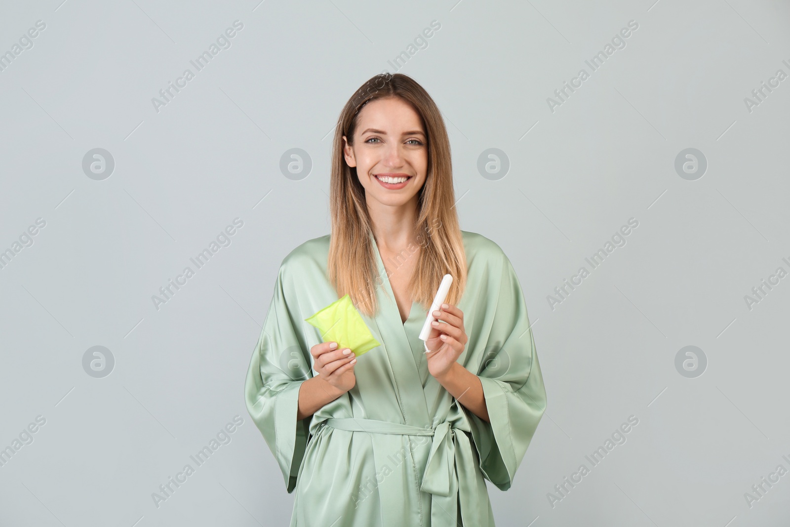 Photo of Happy young woman with disposable menstrual pad and tampon on grey background