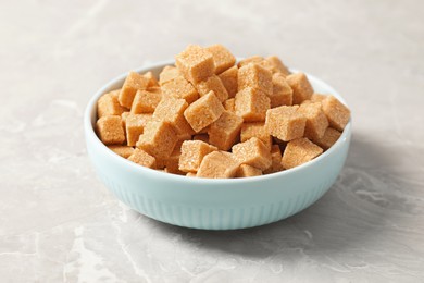 Photo of Brown sugar cubes in bowl on light grey marble table