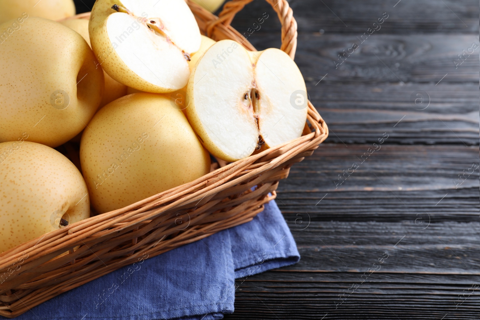 Photo of Cut and whole apple pears in basket on black wooden table, closeup