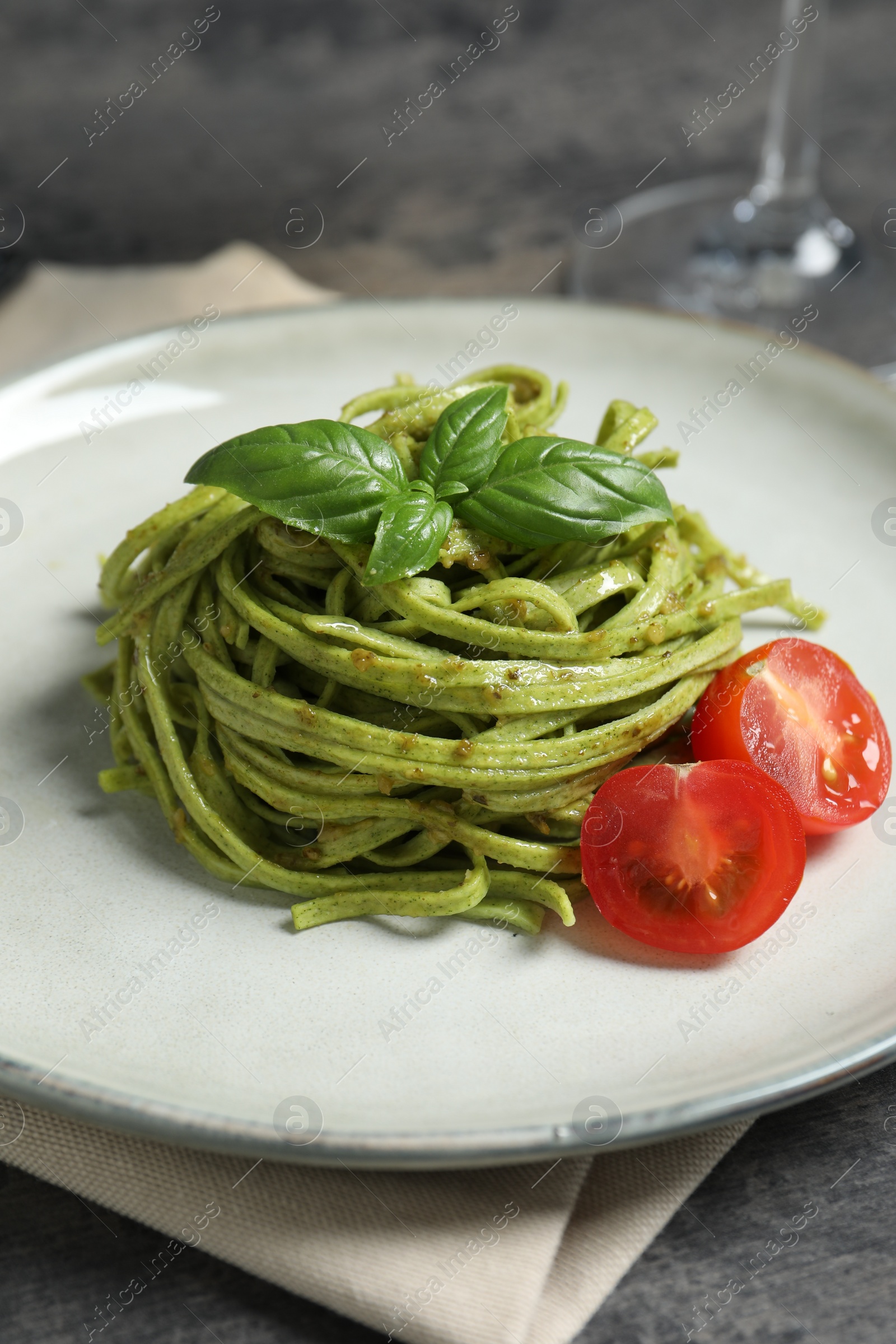 Photo of Tasty tagliatelle with spinach and tomatoes served on grey table, closeup. Exquisite presentation of pasta dish