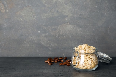 Glass jar with pine nuts on table against  gray background. Space for text