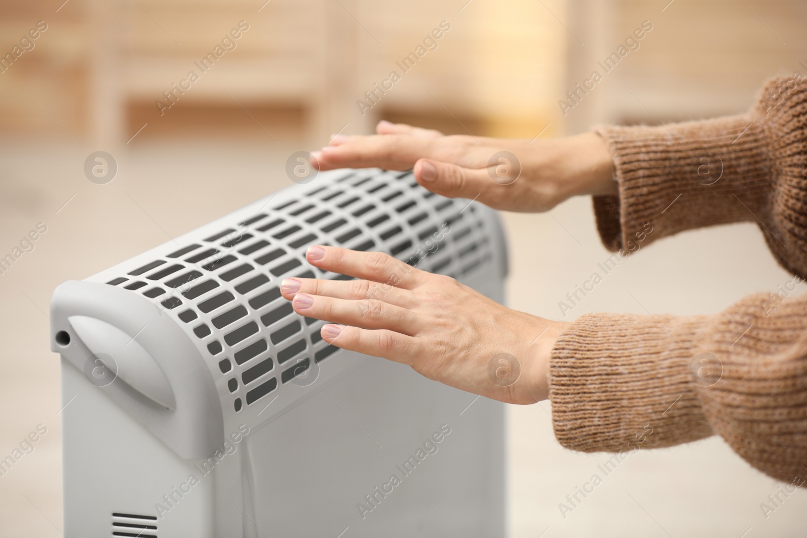 Photo of Woman warming hands on electric heater at home, closeup