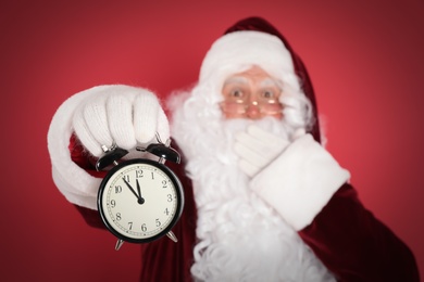 Photo of Santa Claus holding alarm clock on red background, focus on hand. Christmas countdown