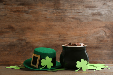 Photo of Pot of gold coins, hat and clover leaves on wooden table, space for text. St. Patrick's Day celebration