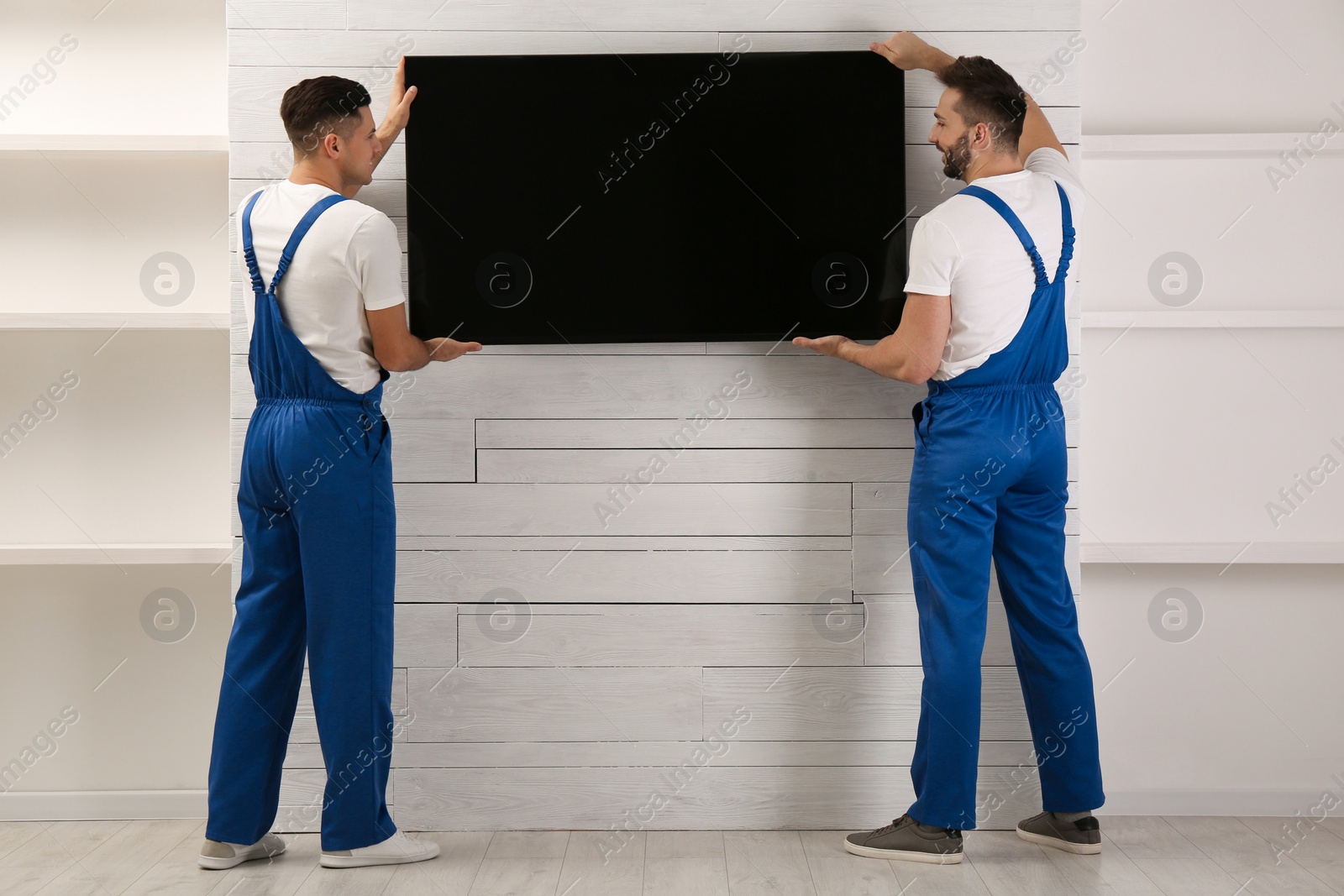 Photo of Professional technicians installing modern flat screen TV on wall indoors