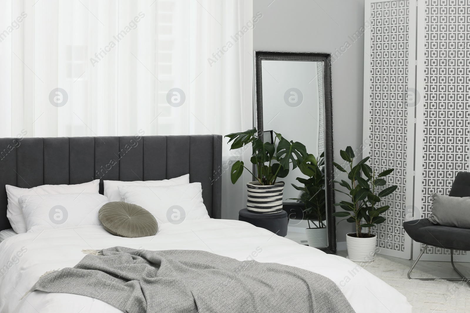 Photo of Large comfortable bed and beautiful houseplants in room. Bedroom interior