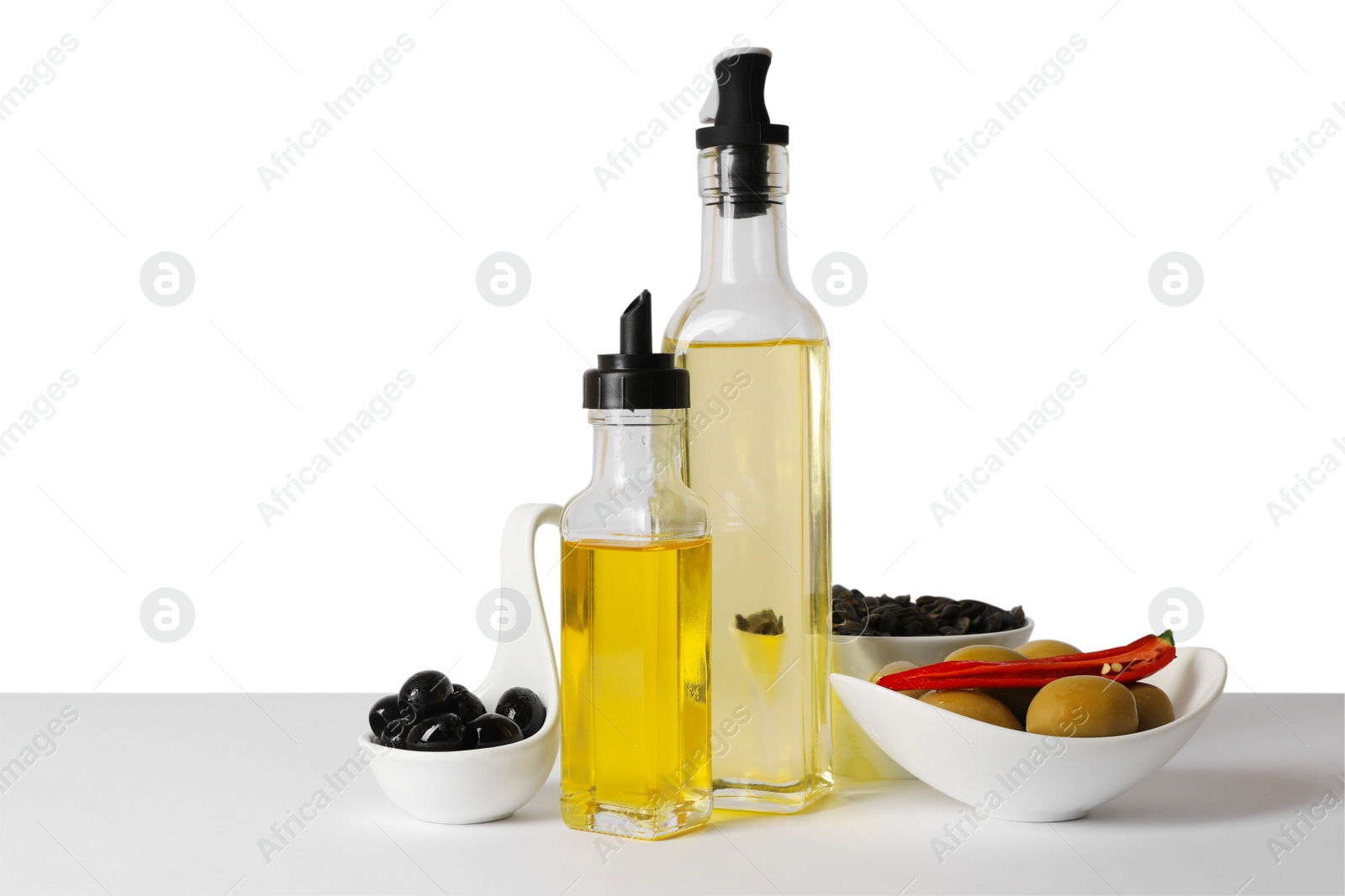 Photo of Bottles of different cooking oils, olives and sunflower seeds on white background